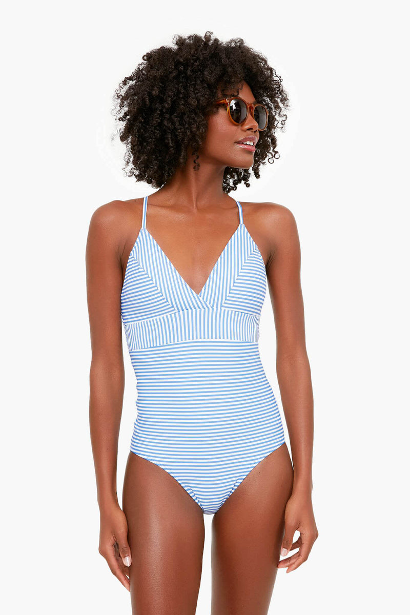 A woman in sunglasses models a stylish Vineyard Vines light blue and white striped one-piece swimsuit, highlighting trendy women's swimwear.