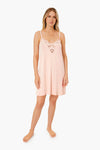 A woman stands barefoot in a light pink Eberjey sleeveless nightdress with botanical lace trim and floral embroidery at the neckline, crafted from lightweight stretch modal for ultimate comfort.
