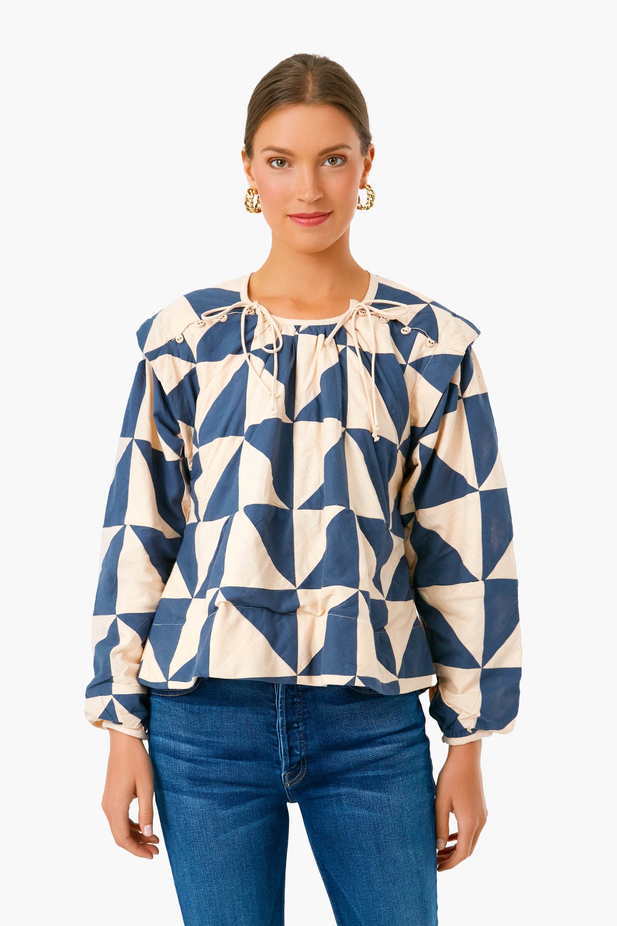 A woman wears a MIRTH blue and beige geometric long-sleeve tie-neck blouse with blue jeans, highlighting artisan-made clothing in an effortlessly chic style.