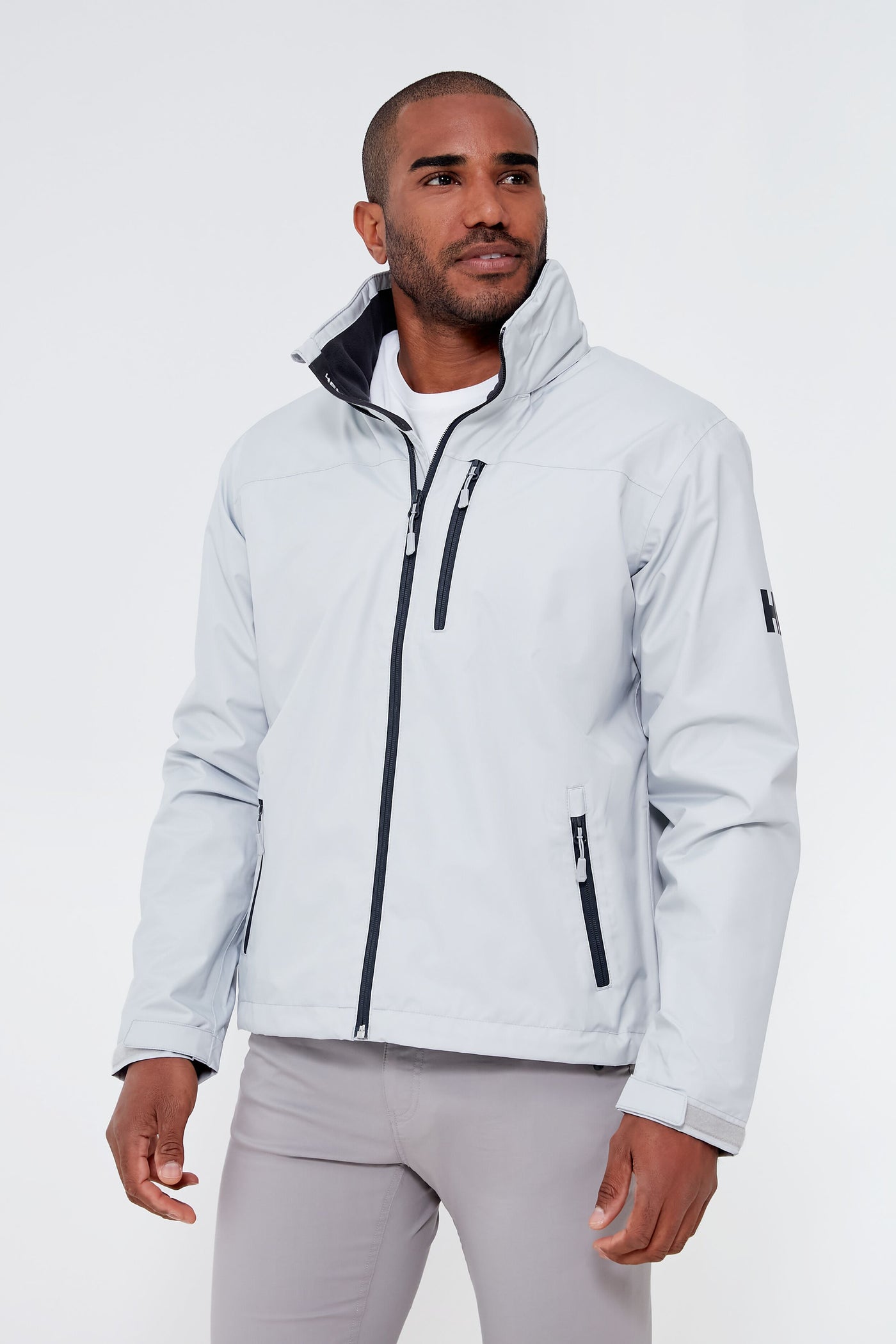 A man wearing a Helly Hansen light gray fleece-lined jacket with black zippers and a high collar over a white shirt.