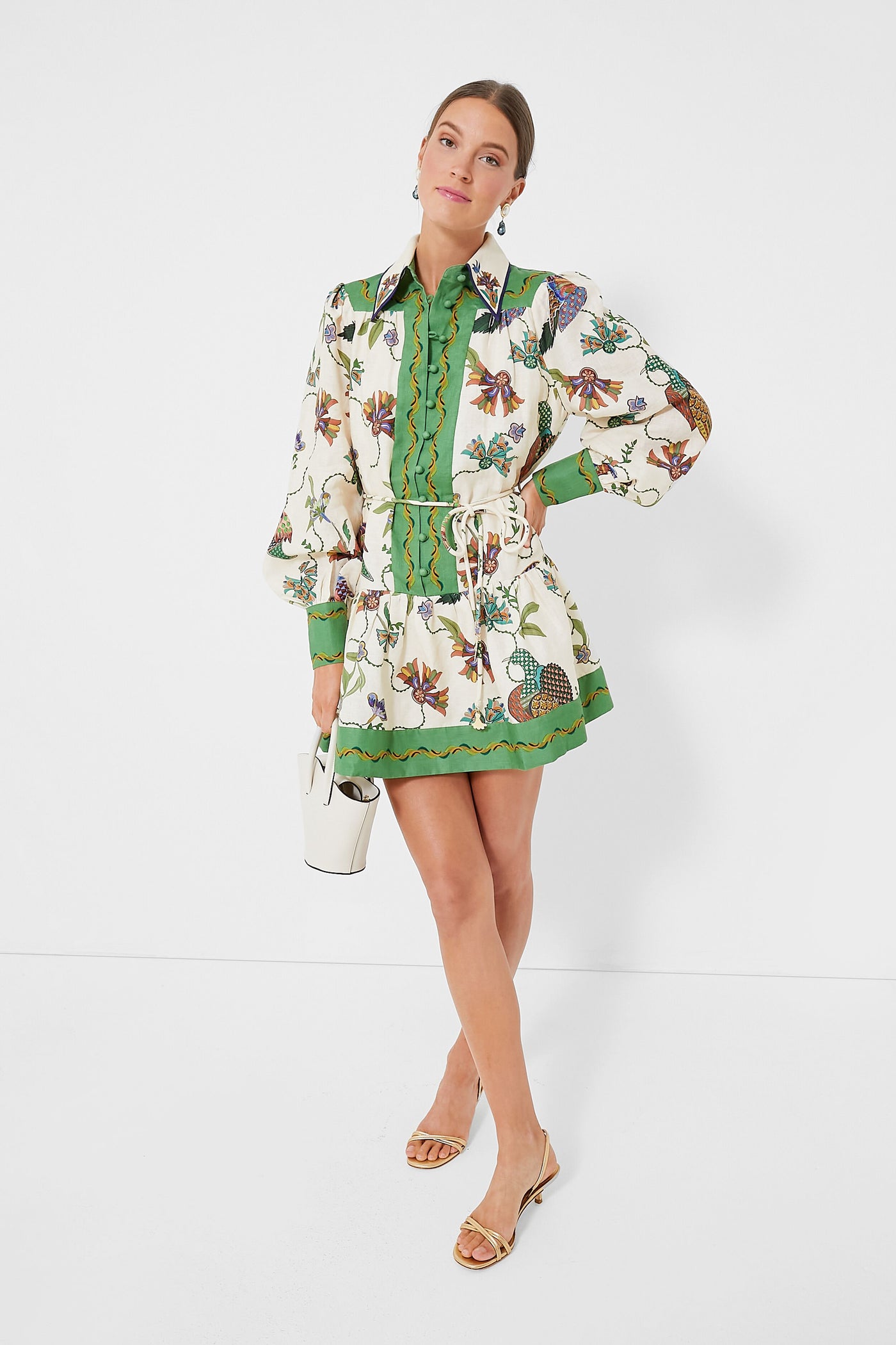A woman wears an Alemais green and white linen mini dress from the contemporary Australian brand, styled with beige sandals and a small white bag.