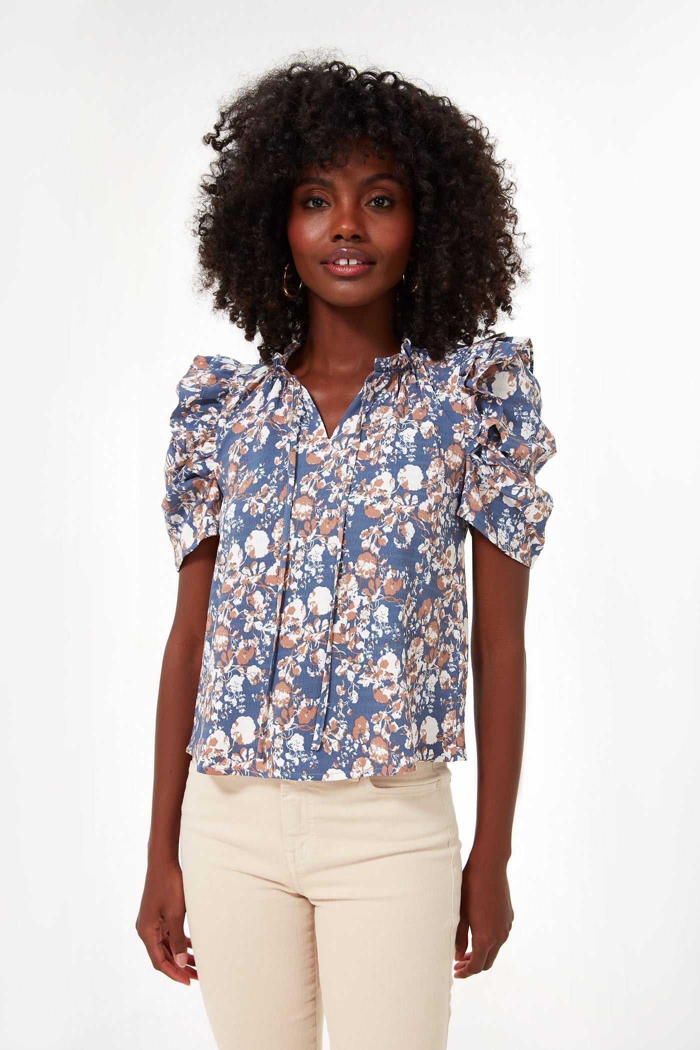 A woman models a fresh, modern look in an En Saison blue floral puff-sleeve blouse paired with light beige pants, highlighting contemporary women's fashion.
