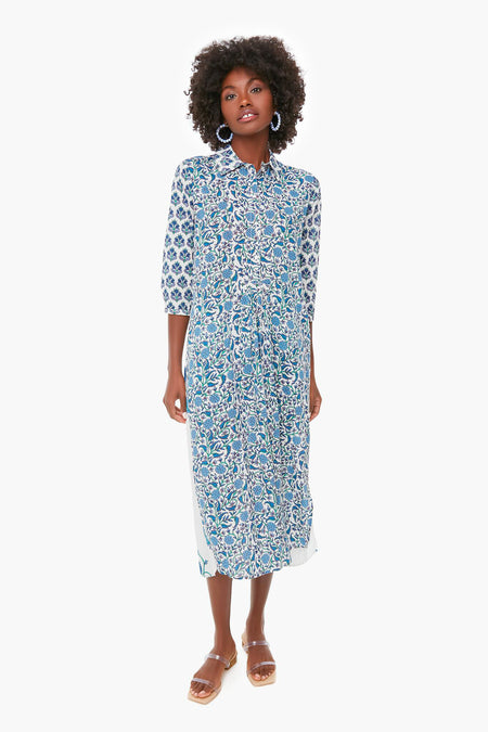 A woman wearing a Ro's Garden blue and white vibrant print midi dress with three-quarter sleeves, hoop earrings, and brown sandals—ideal luxury travel-wear for stylish getaways.