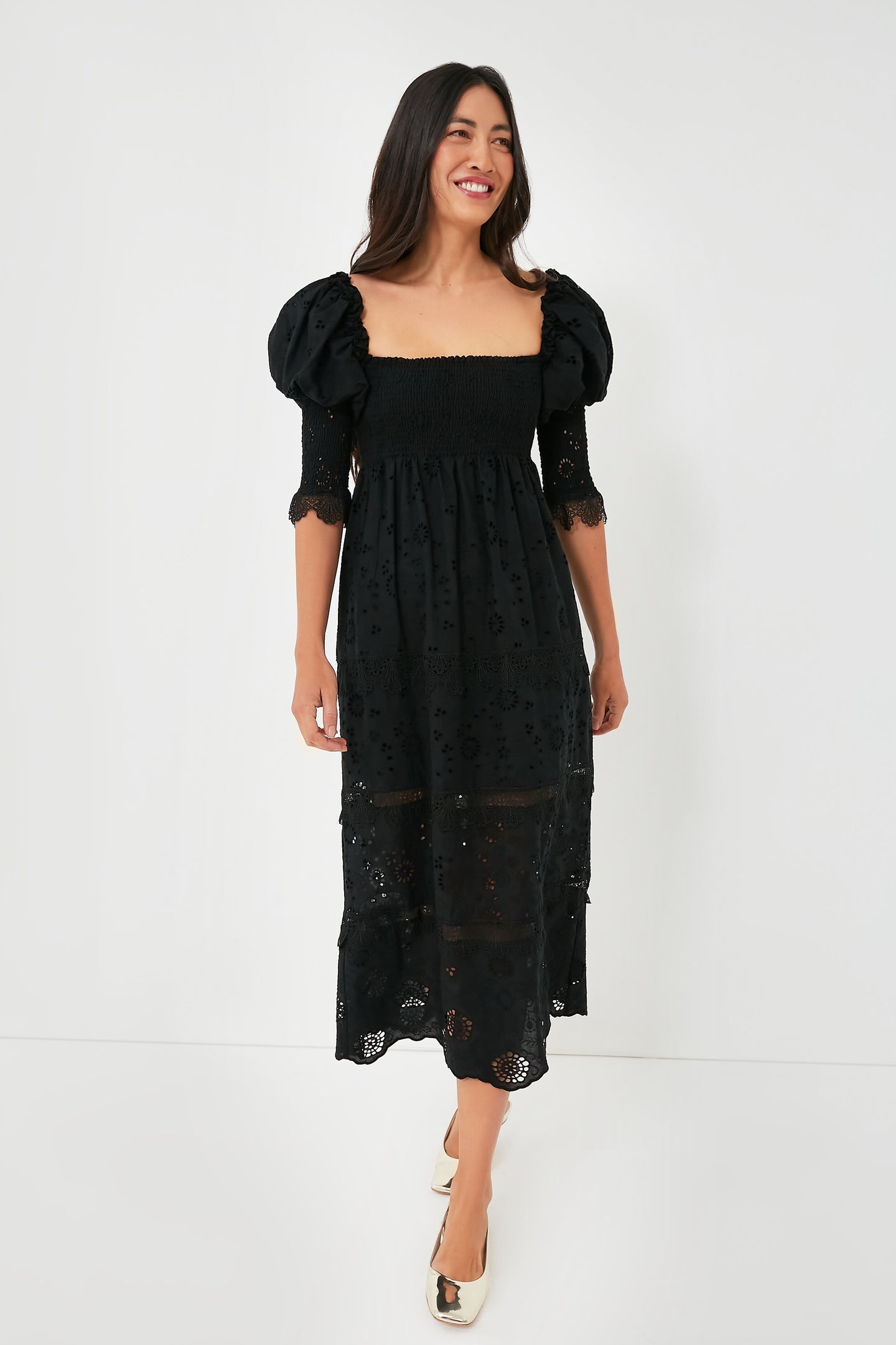 A woman wears the O.P.T Black Wednesday Midi Dress featuring puff sleeves, lace details, a smocked bodice, and eyelet embroidery, styled with cream shoes.