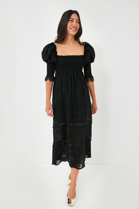 A woman wears the O.P.T Black Wednesday Midi Dress featuring puff sleeves, lace details, a smocked bodice, and eyelet embroidery, styled with cream shoes.