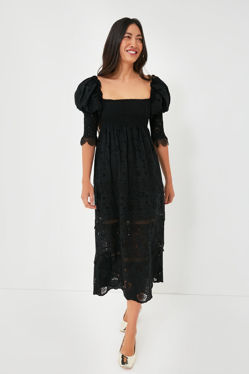 A woman wears the O.P.T Black Wednesday Midi Dress featuring puff sleeves, lace details, a smocked bodice, and eyelet embroidery, styled with cream shoes.