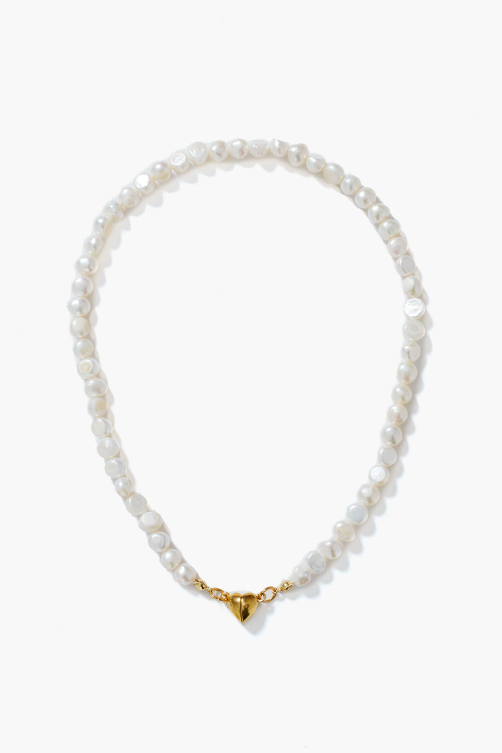 A Petit Moments white pearl necklace with gold-tone hardware and a heart-shaped magnetic closure, elegantly arranged in a circle.