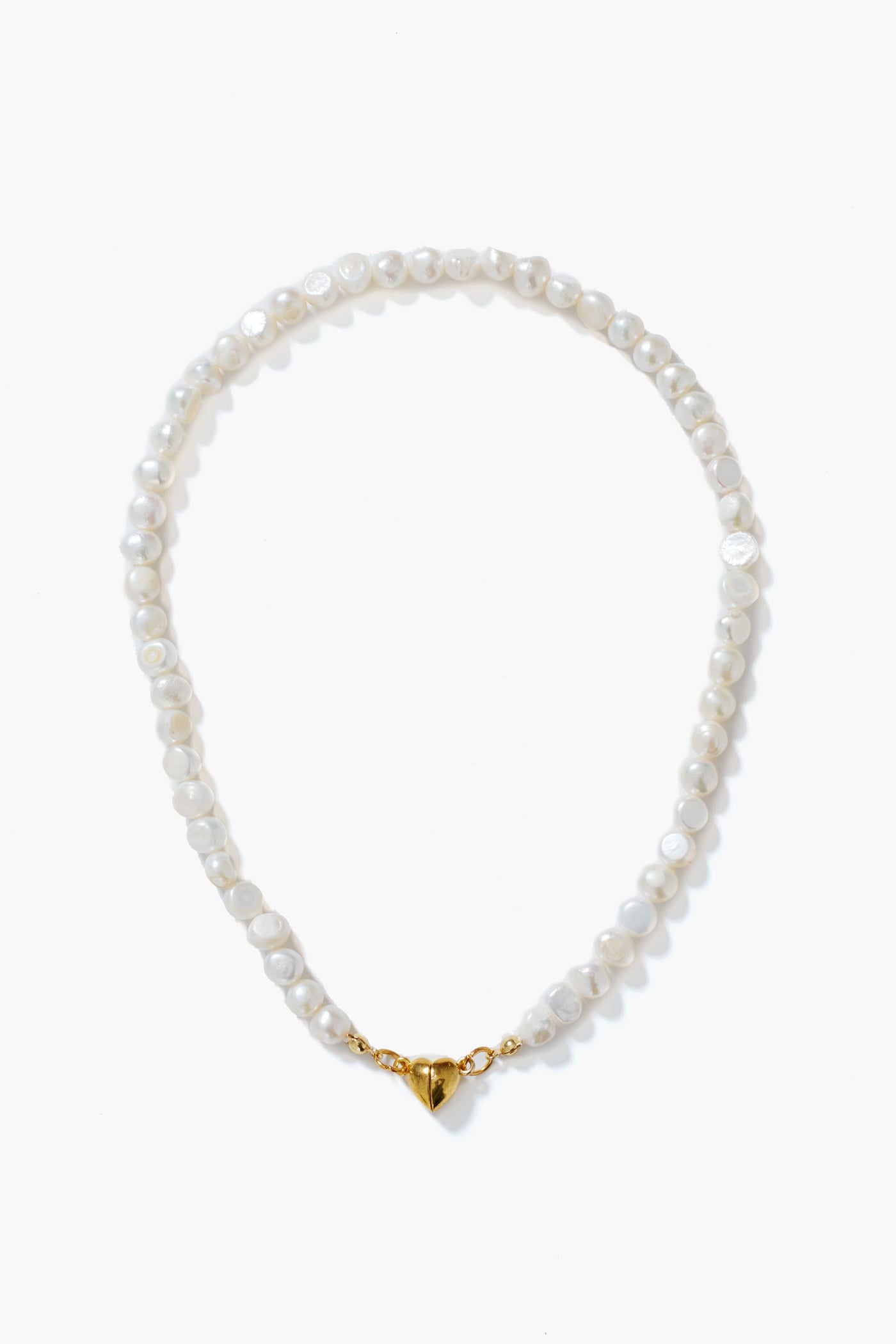 A Petit Moments white pearl necklace with gold-tone hardware and a heart-shaped magnetic closure, elegantly arranged in a circle.