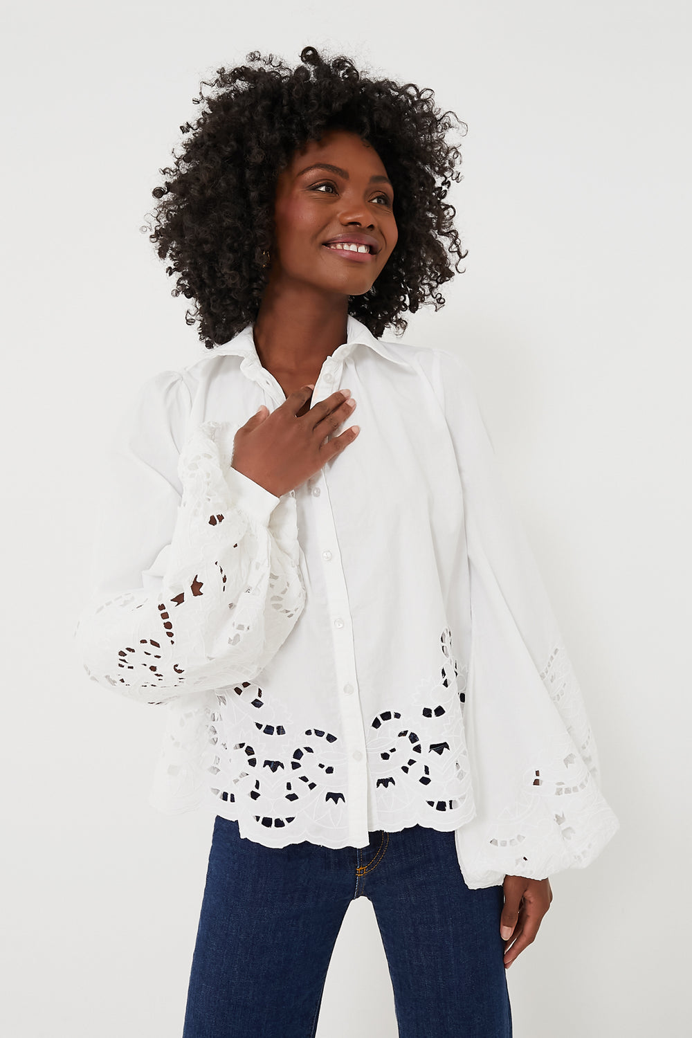 A woman wears a byTiMo white poplin blouse with eyelet lace on the sleeves and hem, paired with dark blue jeans.