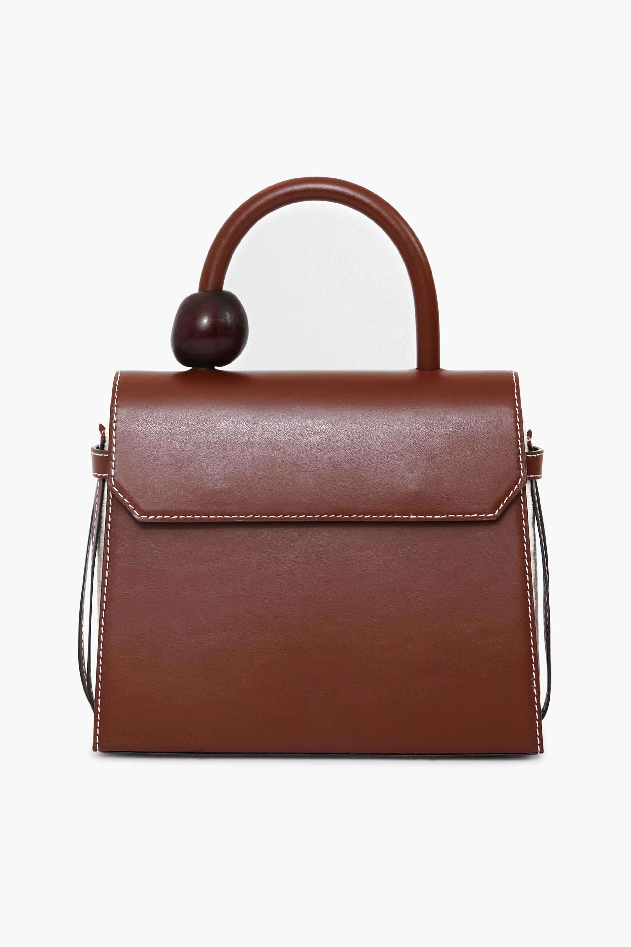 The Ballen bag is crafted from brown structured nappa leather with white stitching, a curved handle with a large round accent, and a flap closure. Luxuriously handmade in Colombia for timeless style.