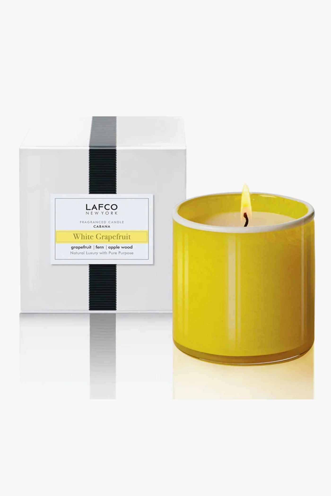 A yellow handblown glass LAFCO New York White Grapefruit Candle burns next to its white box with black detailing, adding a touch of home fragrance.