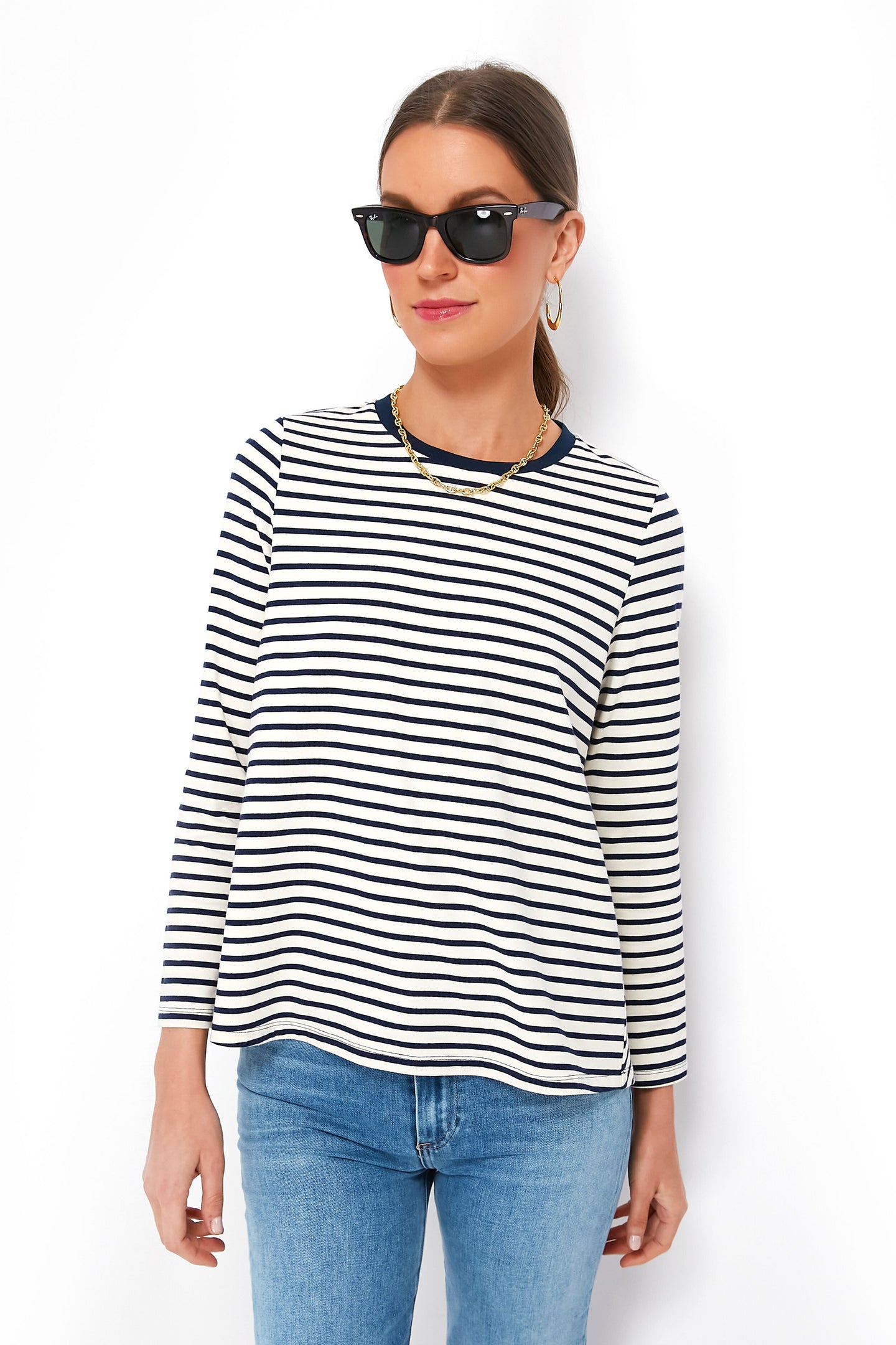 Woman wearing Pomander Place black sunglasses, gold jewelry, a white and navy striped relaxed-fit long sleeve tee in soft cotton blend, and blue jeans.