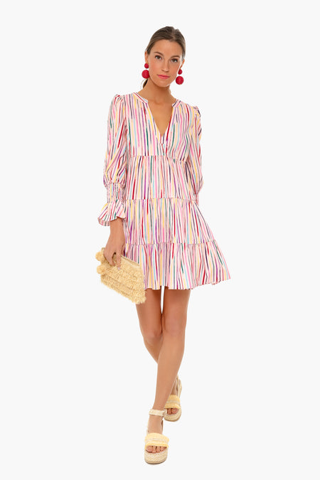 Woman wearing a long-sleeve Pomander Place dress with rainbow stripes, holding a woven clutch, paired with platform sandals and large red earrings.