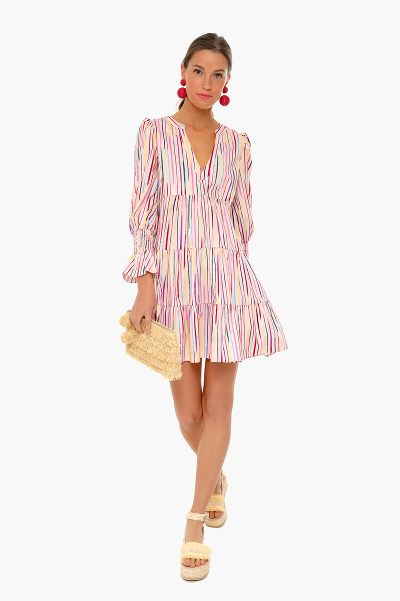 Woman wearing a long-sleeve Pomander Place dress with rainbow stripes, holding a woven clutch, paired with platform sandals and large red earrings.