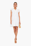 A woman wears a Sea New York white ruffled cotton dress with button-downs, tan platform sandals, large gold earrings, and holds a small woven clutch—perfect for resort style.