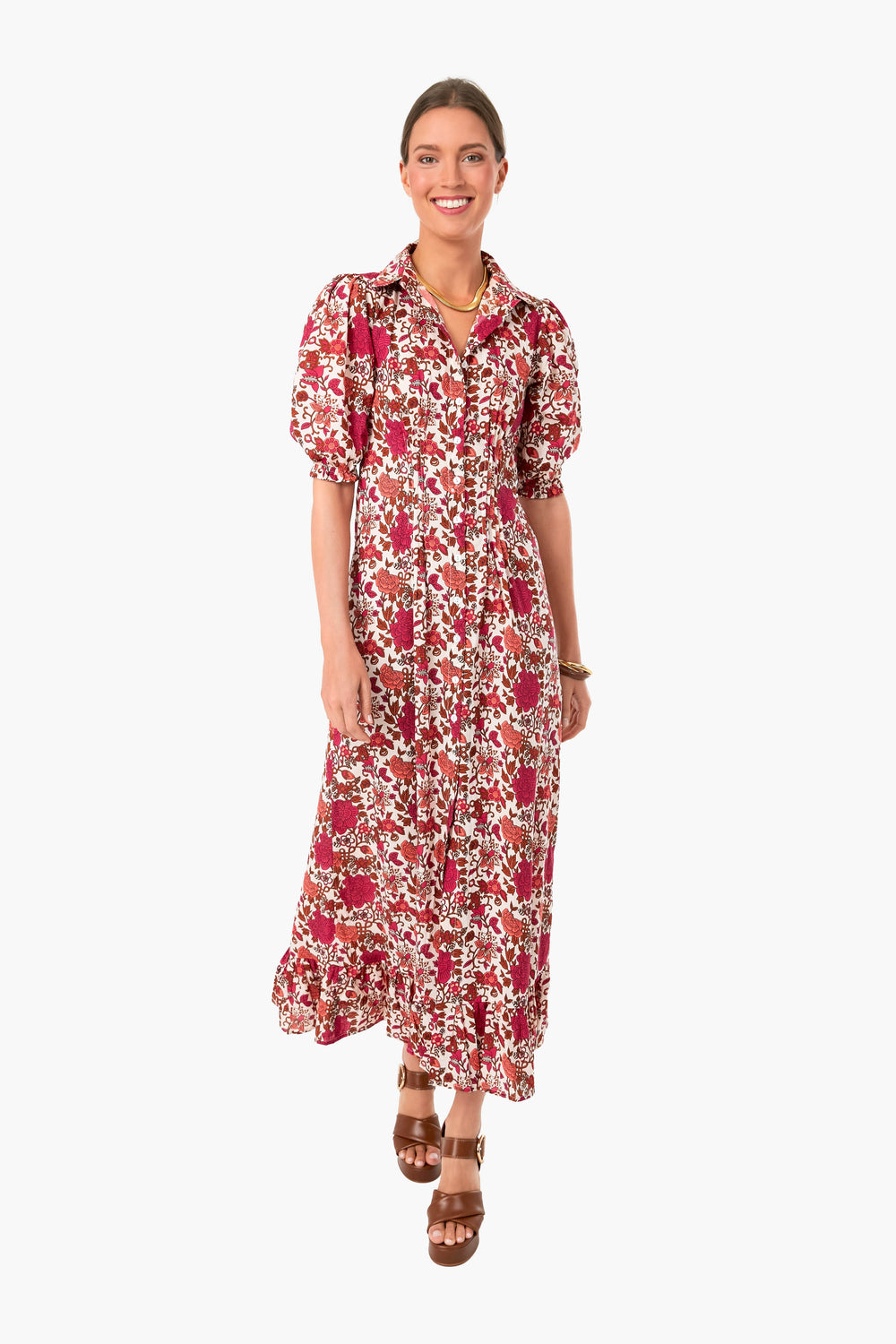 A woman smiles in the Mille Pondicherry Laurel Dress, a red and white floral shirtdress with puff sleeves and a ruffled hem, styled with brown sandals and gold jewelry for an effortlessly chic boho look.