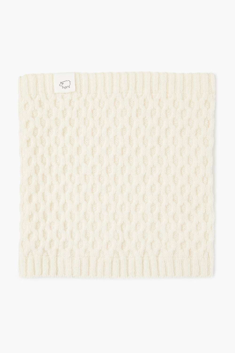 A cream-colored, knitted cormo wool neck gaiter from baa with a ribbed edge and a small white tag featuring a line drawing of a sheep.