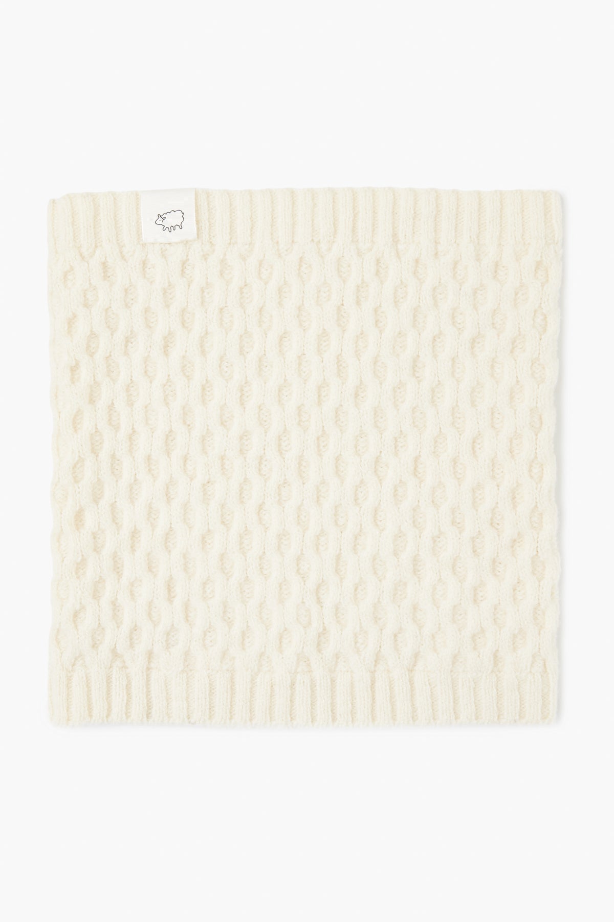 A cream-colored, knitted cormo wool neck gaiter from baa with a ribbed edge and a small white tag featuring a line drawing of a sheep.