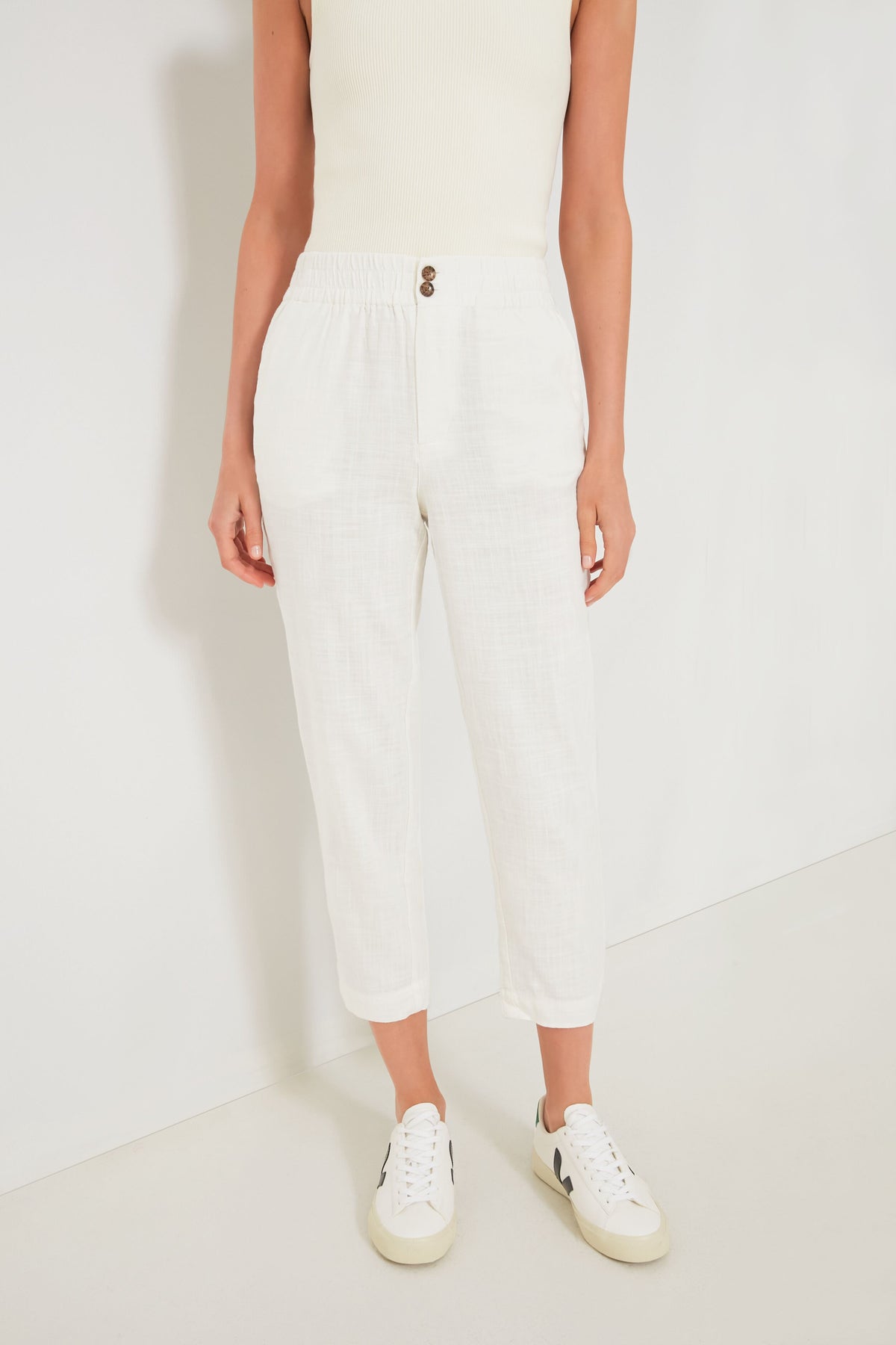 A person wears a Marine Layer sleeveless white top, ultra-soft white trousers with an elastic waistband and buttons, and white sneakers for a fresh, casual look.