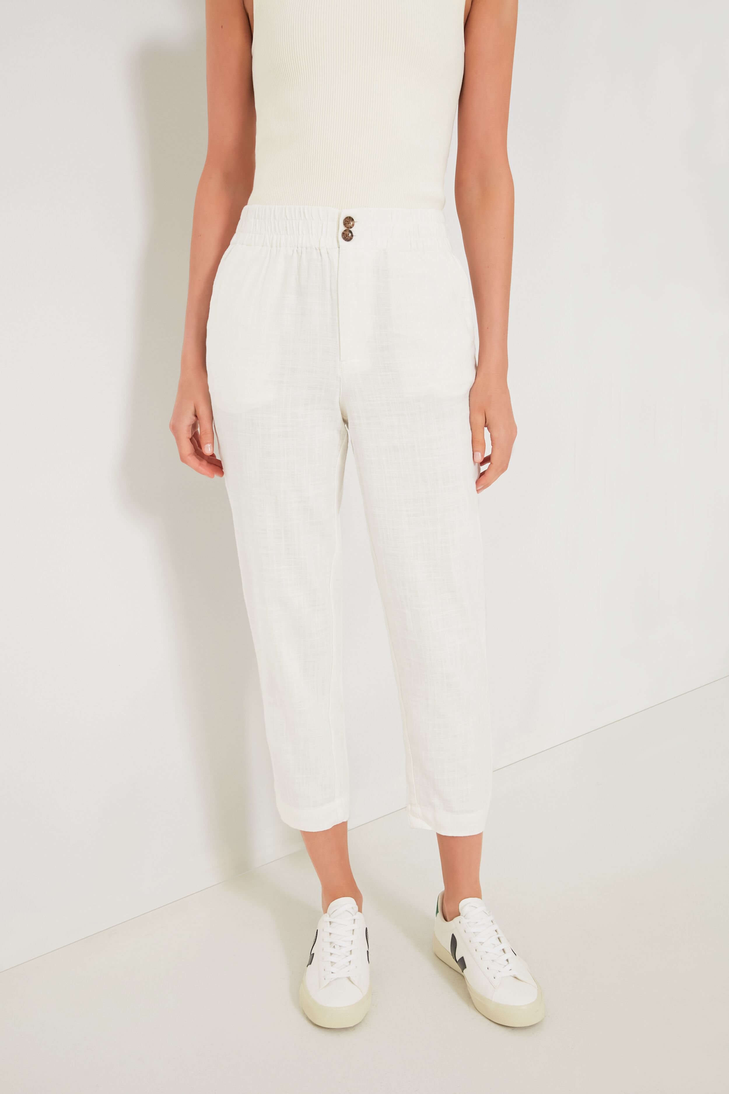 A person wears a Marine Layer sleeveless white top, ultra-soft white trousers with an elastic waistband and buttons, and white sneakers for a fresh, casual look.