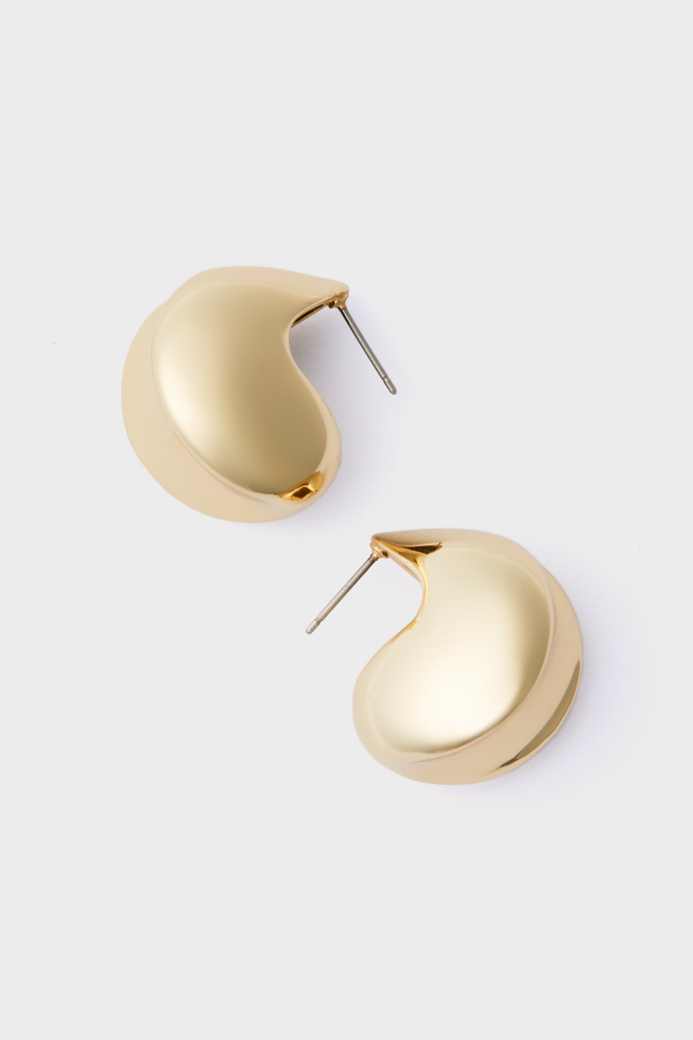 A pair of shiny, high-polish gold chunky hoop earrings from Jenny Bird with a smooth, curved design displayed on a light gray background—perfect as standout fashion jewelry.