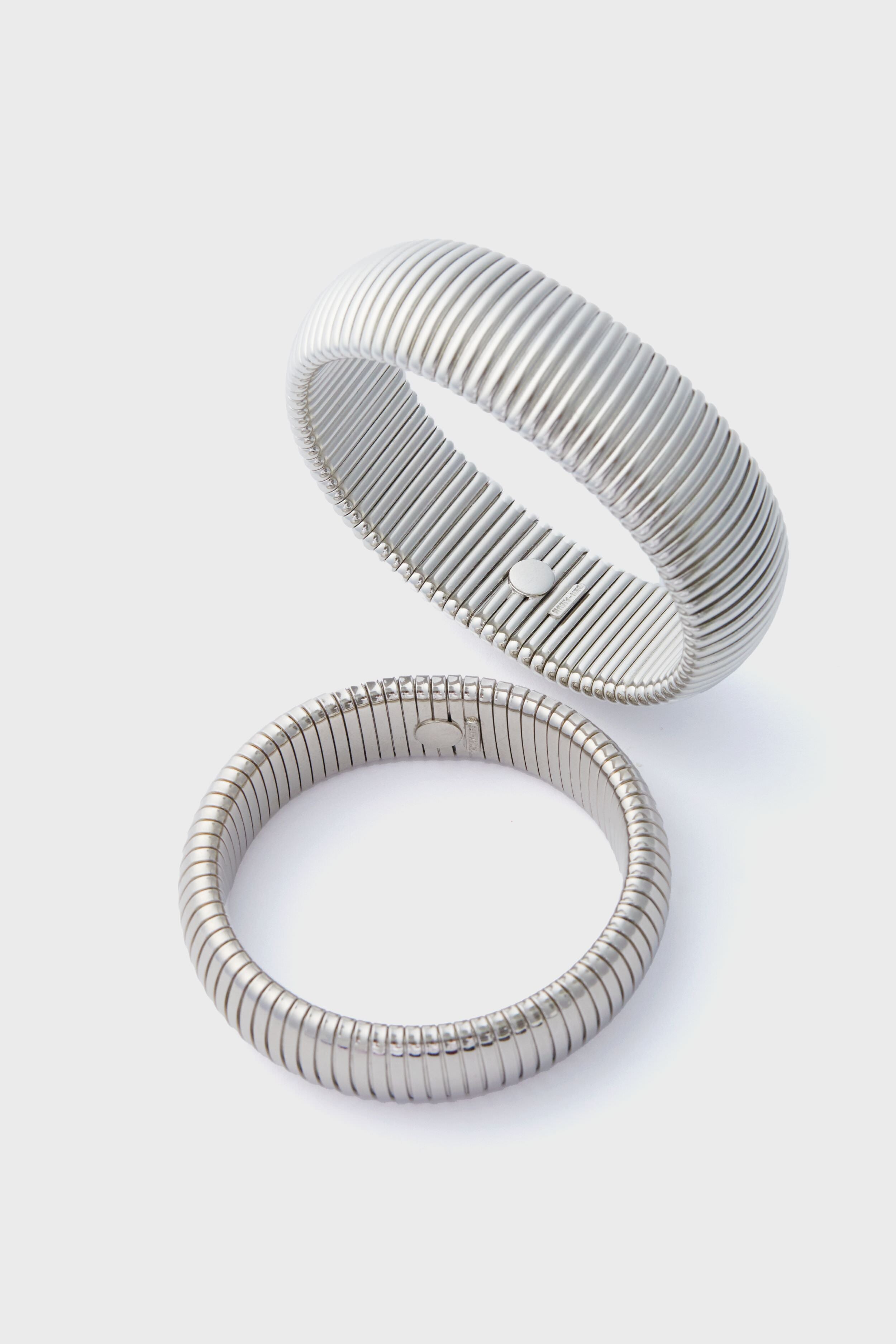 Two silver alloy bangles with ribbed designs are shown, one upright and one flat. These Ben Amun Silver Cobra Bracelets showcase elegant craftsmanship and make bold statement jewelry pieces.