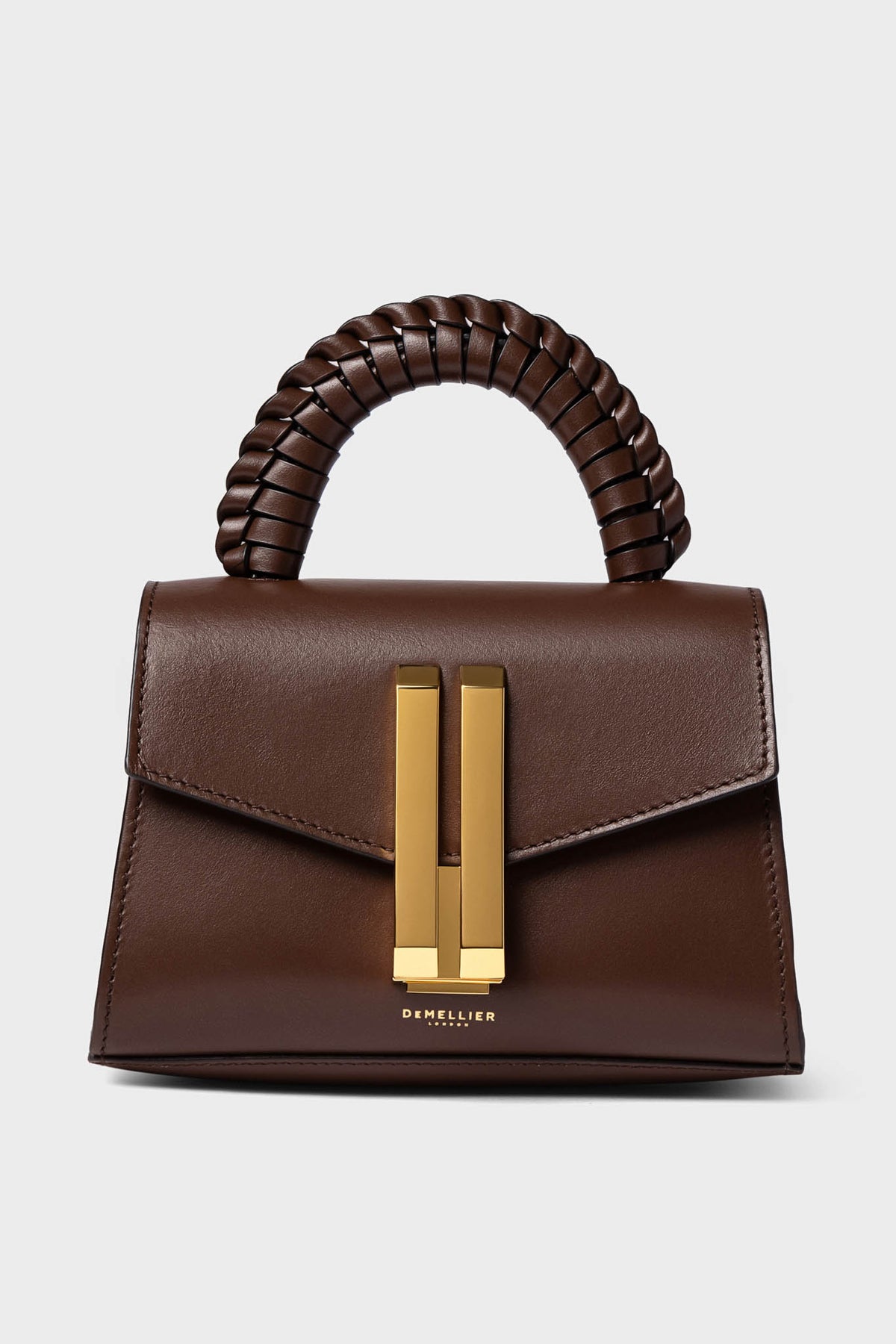 A small brown handcrafted leather purse by Demellier with a braided handle, gold rectangular clasp, and the brand logo on the front. This elegant micro-bag adds sophistication to any outfit.