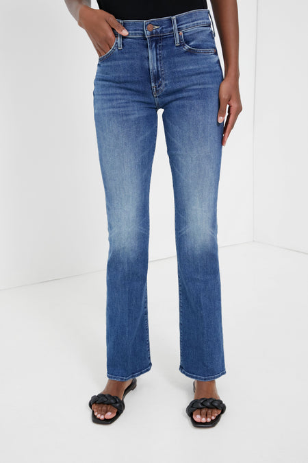 Person wears high-waisted, narrow flared jeans in indigo wash by MOTHER with black sandals. Only the lower body is shown.