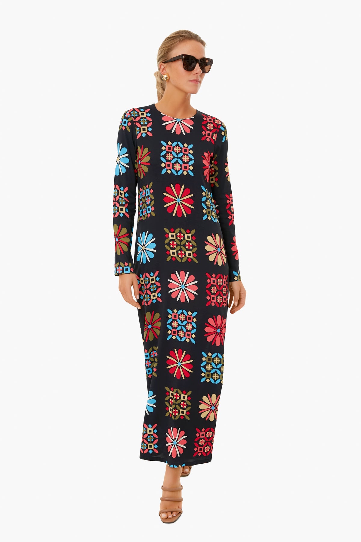 A woman models an ankle-length, long-sleeve black swing dress with colorful geometric and floral patterns by La DoubleJ, paired with sunglasses, earrings, and sandals—a standout piece inspired by Italian fashion.