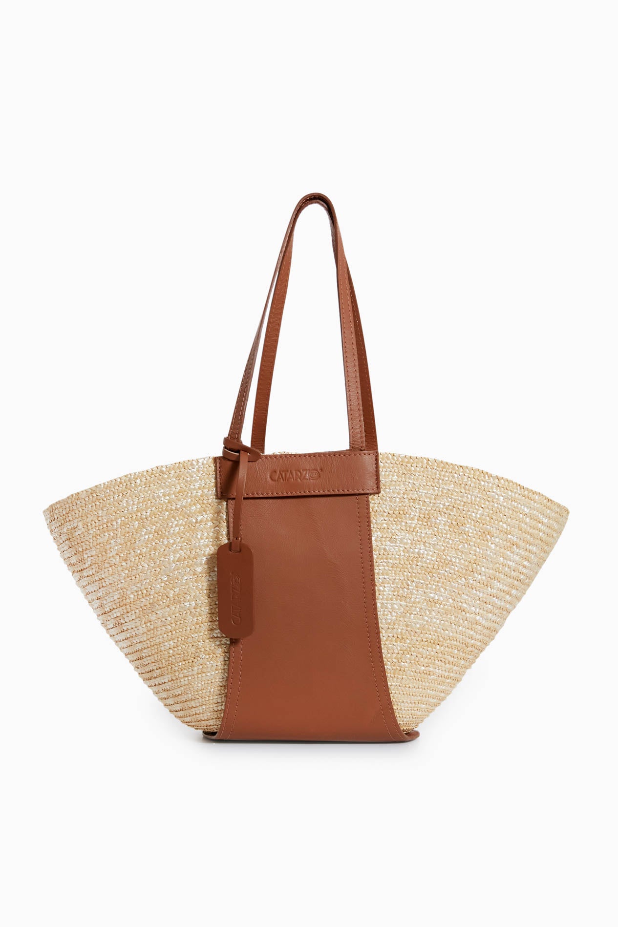 The Catarzi 1910 woven straw tote bag is handmade in Italy with brown leather handles, a leather vertical accent, and a leather tag attached to one handle.