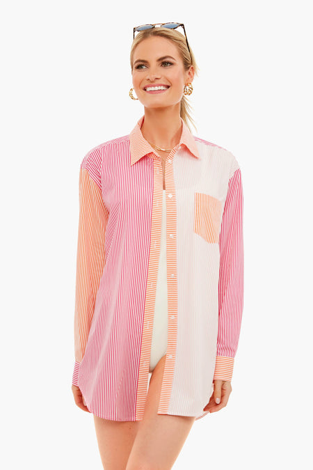 A woman wearing a Solid & Striped long-sleeve, multicolored striped oxford tunic with gold hoop earrings and sunglasses on her head stands smiling.