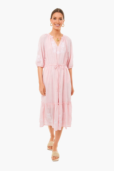 A woman smiles in a Draper James pink embroidered floral midi dress with a drawstring waist and ruffled hem, styled with gold jewelry and beige woven sandals, embodying classic Southern elegance.