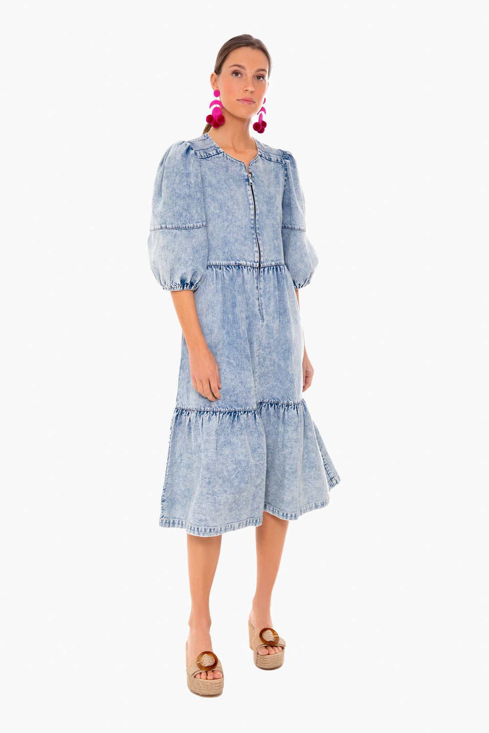 A woman in a Sea New York vintage-inspired puff sleeve midi dress with ruffled tiers, pink pom-pom earrings, and tan platform sandals stands confidently.