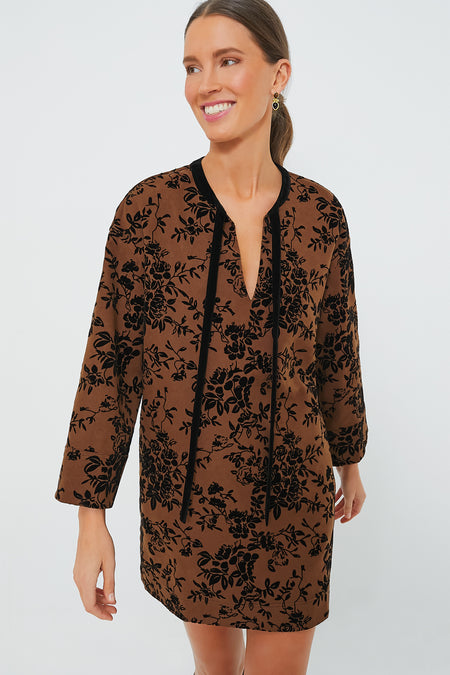 A woman wears a Hyacinth House long-sleeve brown burnout floral mini dress featuring black patterns, velvet ties, and a V-neckline.