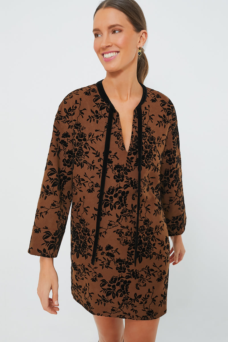 A woman wears a Hyacinth House long-sleeve brown burnout floral mini dress featuring black patterns, velvet ties, and a V-neckline.