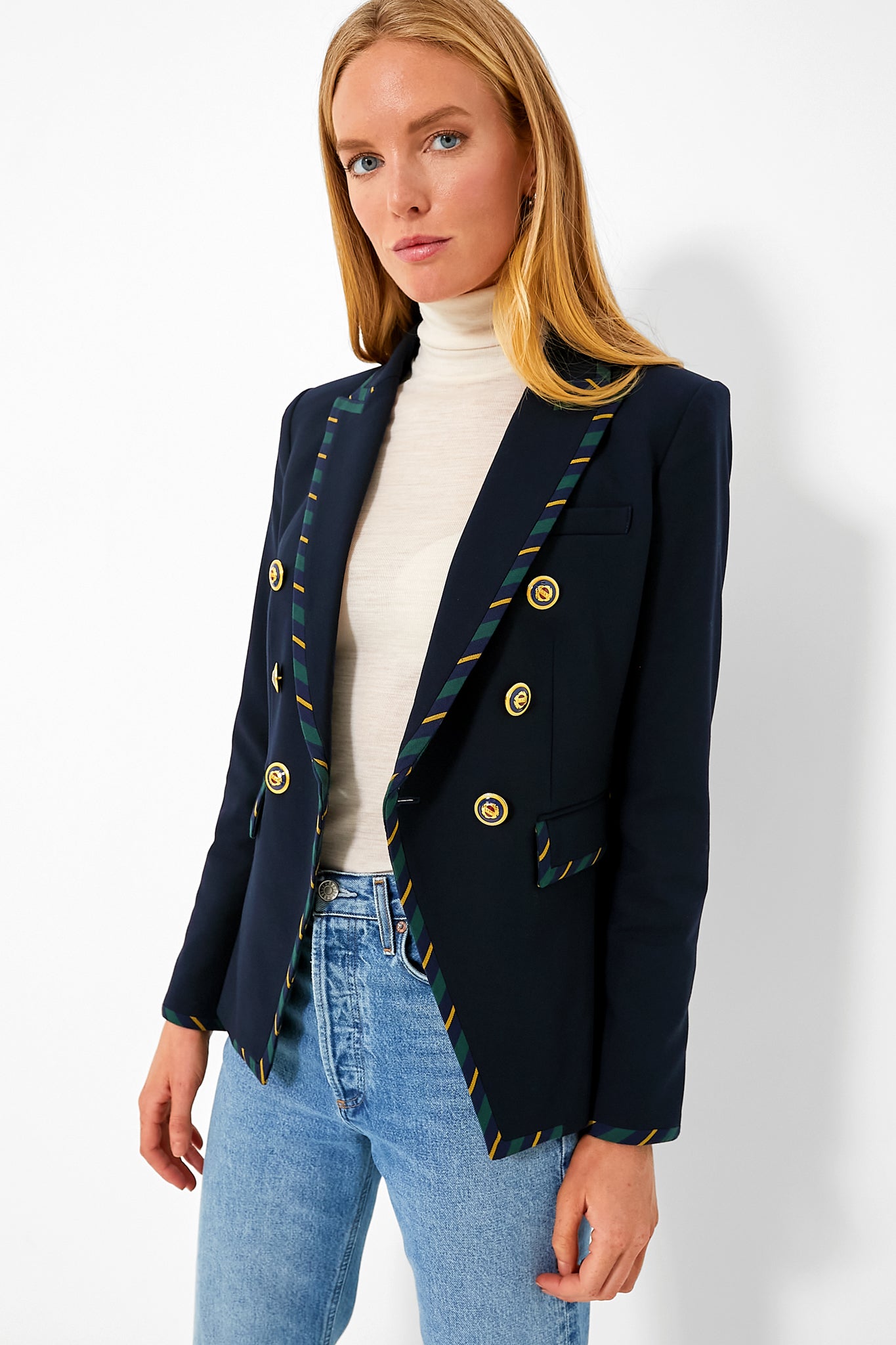 A woman wears a navy stripe Miller Dickey Jacket by Veronica Beard, featuring gold buttons and striped trim, styled with a white turtleneck and blue jeans.