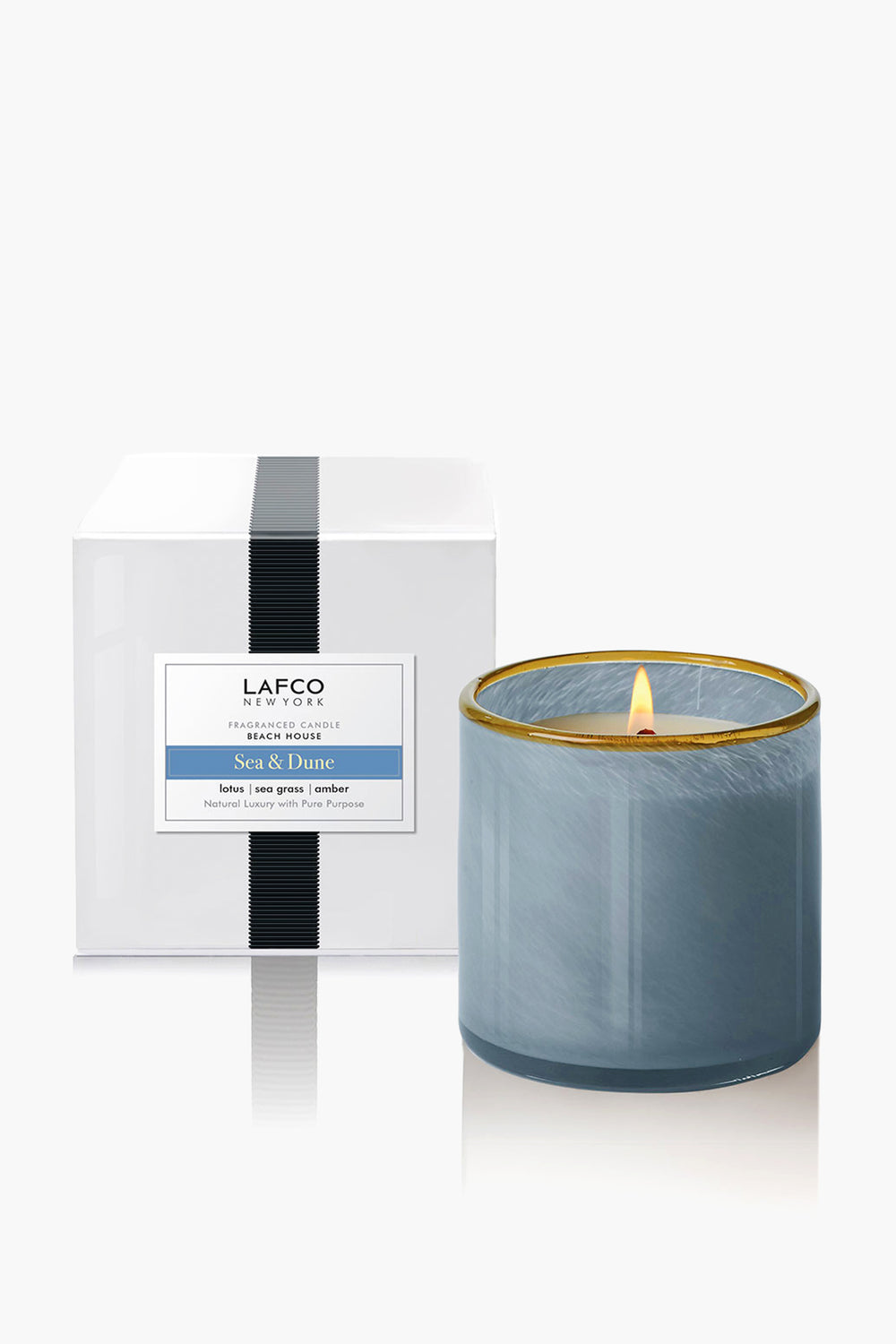 A LAFCO New York Sea & Dune candle in blue hand-blown glass is lit beside its white box, showcasing sophisticated home fragrance.