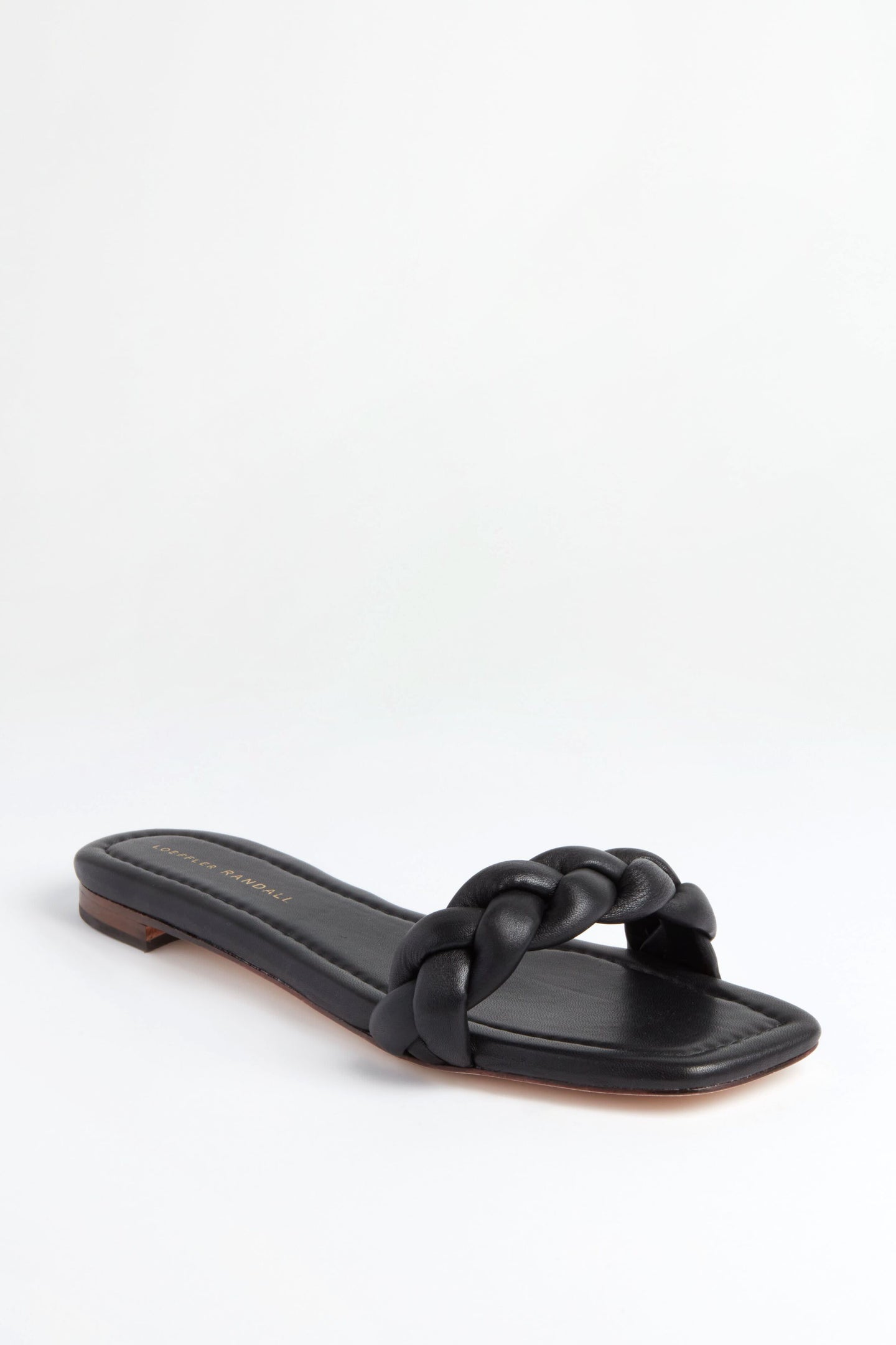 The Loeffler Randall black flat sandal features a single wide braided strap across the foot and a square toe, highlighting the brand's signature elegance.