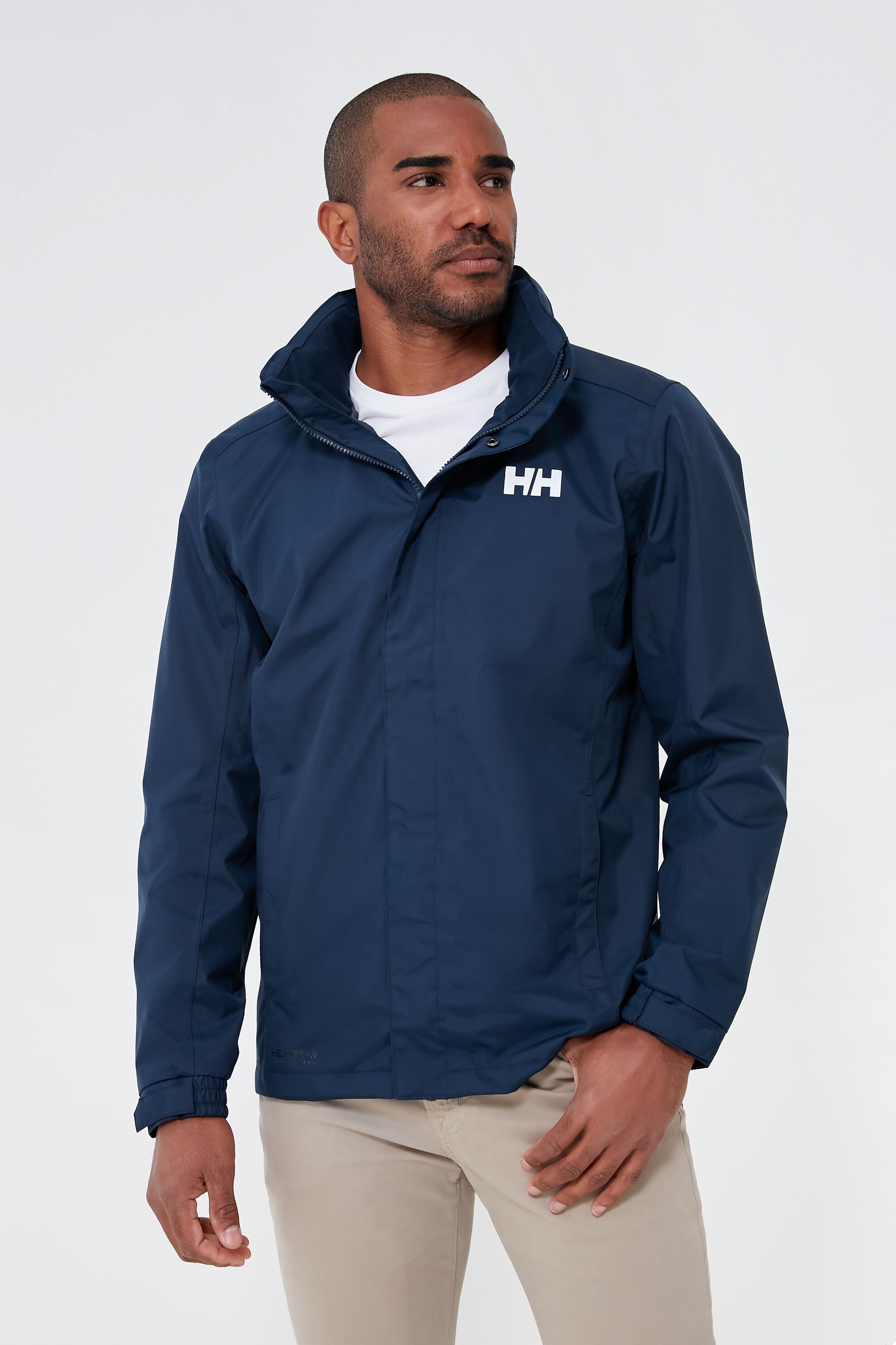 A man wears a Helly Hansen navy waterproof jacket over a white shirt and beige pants.
