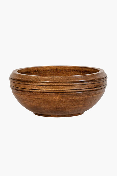 The Juliska mango wood serving bowl features a round, shallow design with a smooth finish and subtle horizontal grooves near the rim, offering an artisanal touch.