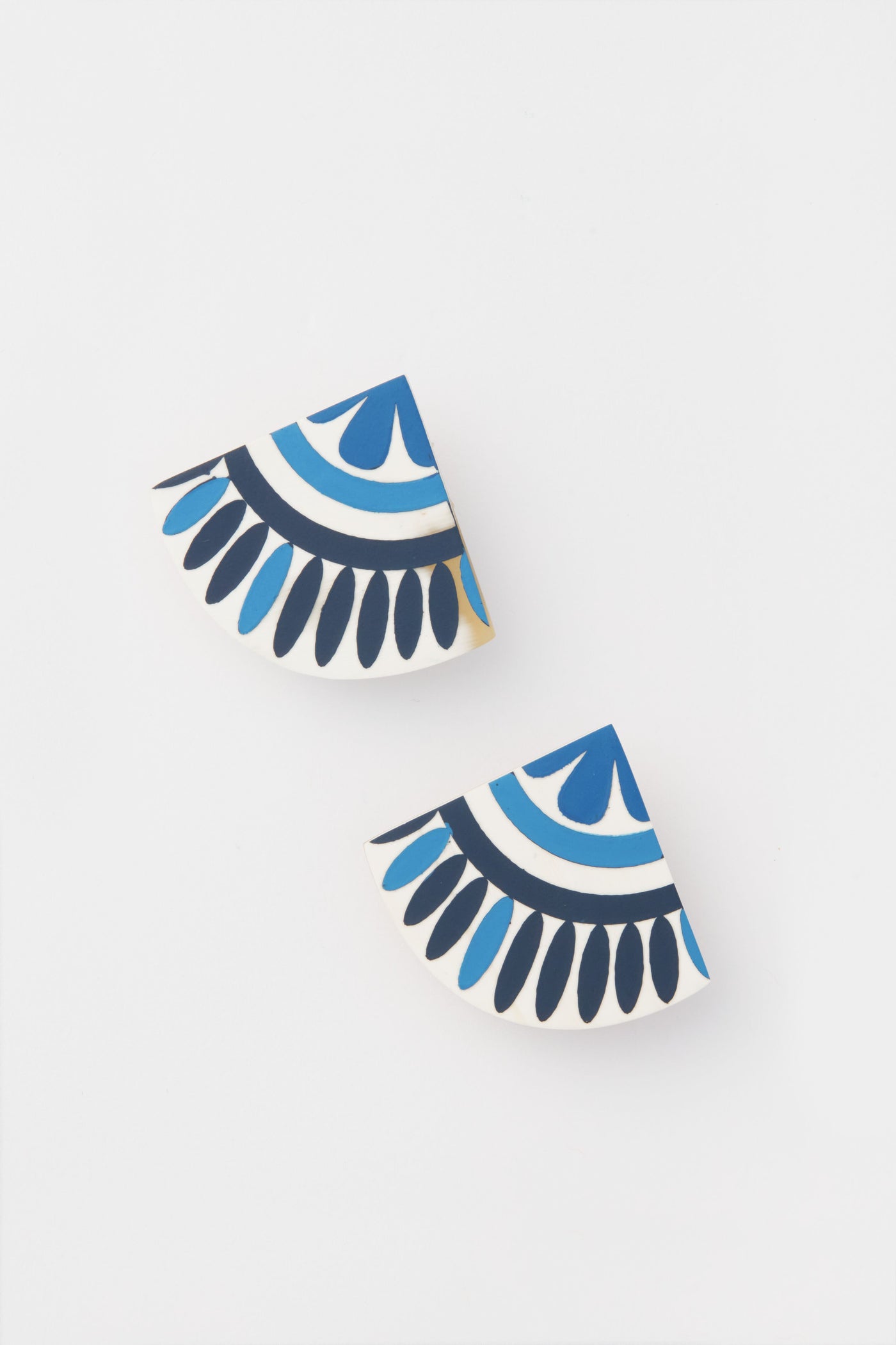 Sunshine Tienda offers lightweight earrings crafted from buffalo horn, featuring two semi-circular shapes adorned with blue, black, and white geometric patterns for a unique look.