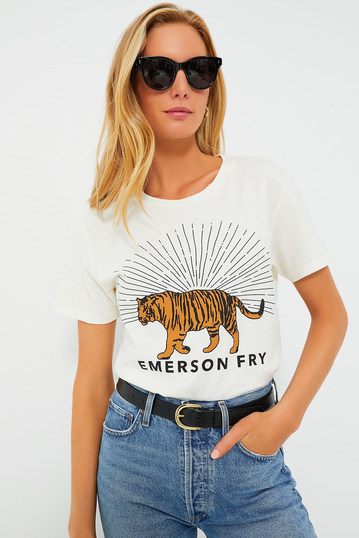 A woman wears sunglasses and the Ivory Tiger Tee by Emerson Fry—a vintage graphic tee with a tiger and EMERSON FRY text—paired with blue jeans and a black belt.