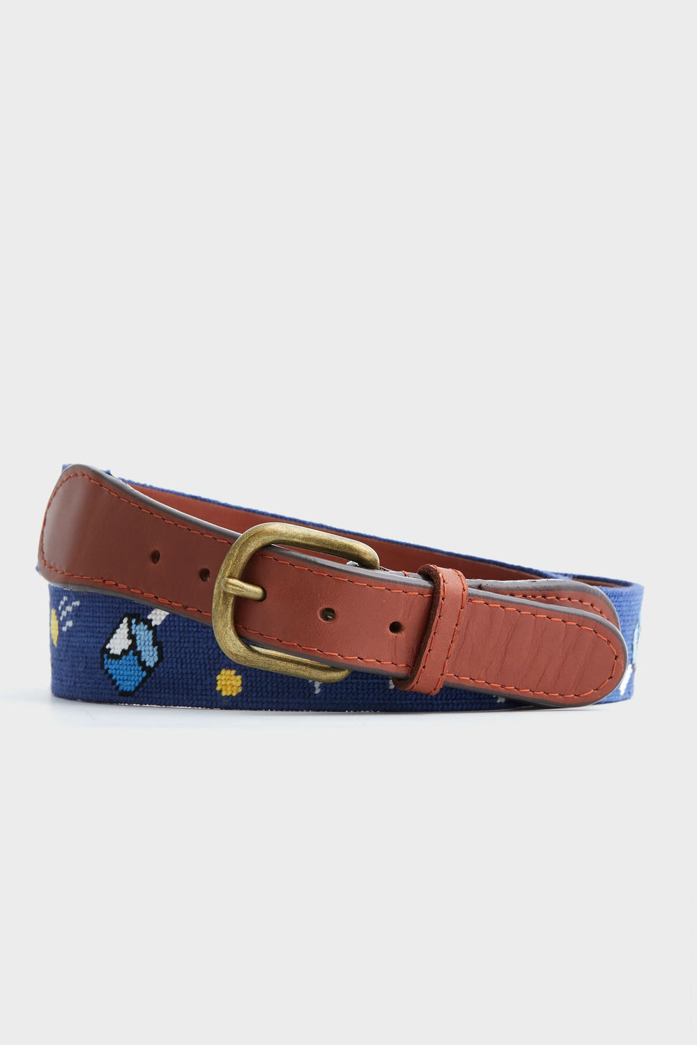 A coiled Smathers and Branson blue hand-stitched needlepoint belt features embroidered designs, brown leather accents, and a brass buckle.