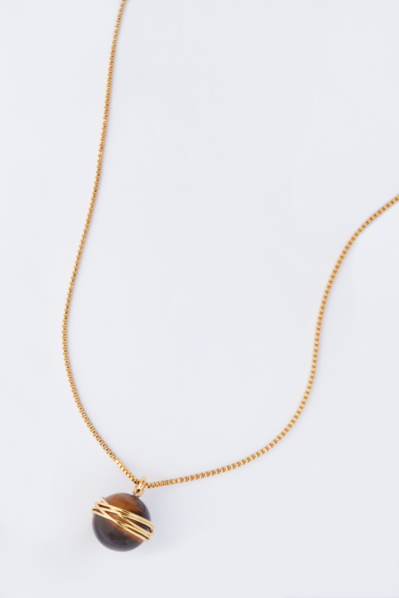 This Tuckernuck Jewelry gold chain necklace showcases a round dark stone pendant wrapped in gold wire, blending vintage inspiration with elegance and timeless charm.
