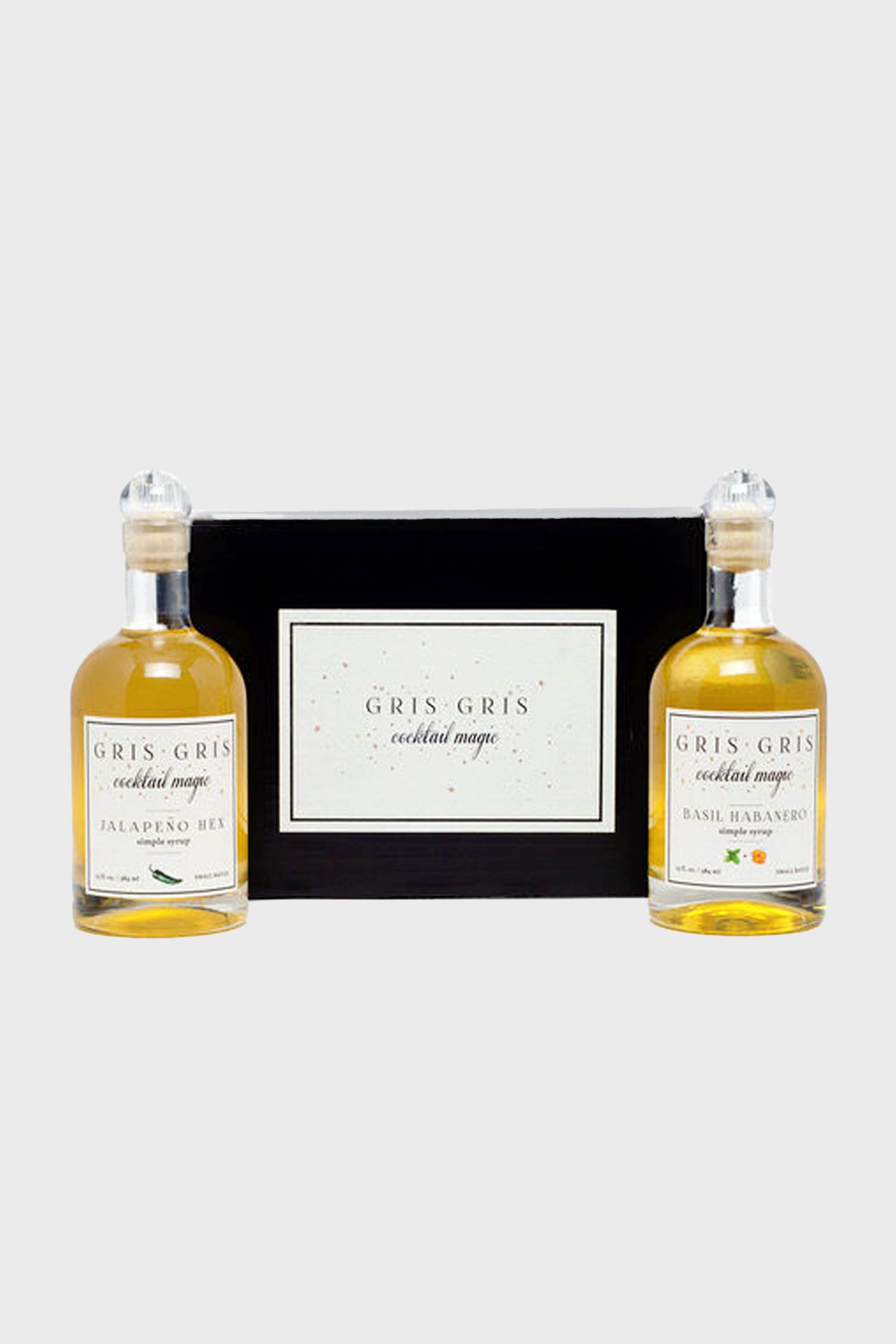 Two bottles of Gris Gris Cocktail Magic mixers, Jalapeño Hex and Basil Habanero, are displayed next to a black Gris Gris Cocktail Magic box—an ideal Spicy Hostess Set featuring craft cocktail syrups for bold drinks.