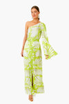 A woman wears the ALEXIS Bliss Lio Dress, a green and white one-shoulder maxi with flared sleeve and waist tie, styled with gold sandals and statement earrings for timeless womenswear elegance.
