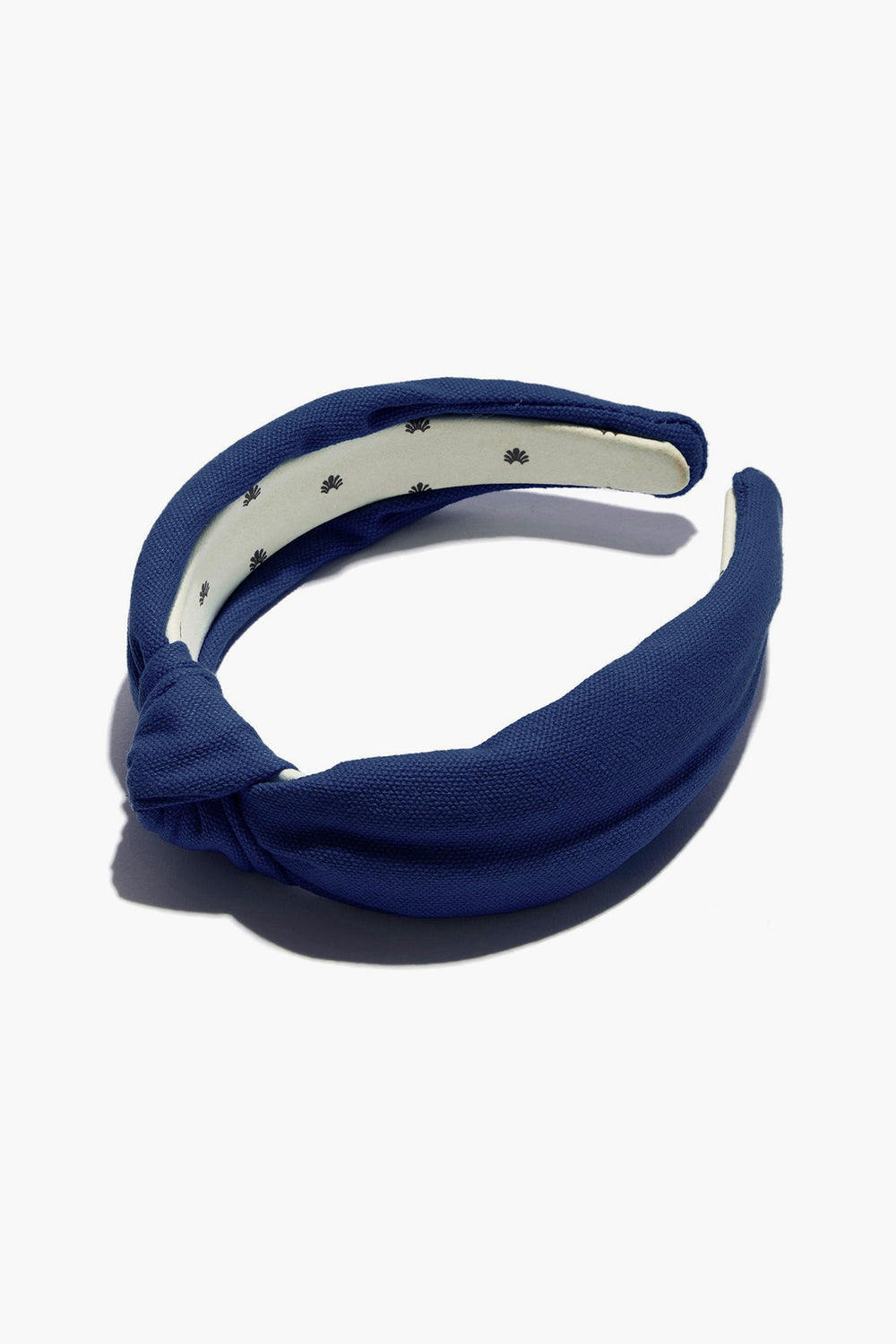 A blue cotton headband by Lele Sadoughi with a woven knotted design and a white inner lining adorned with small black flowers.