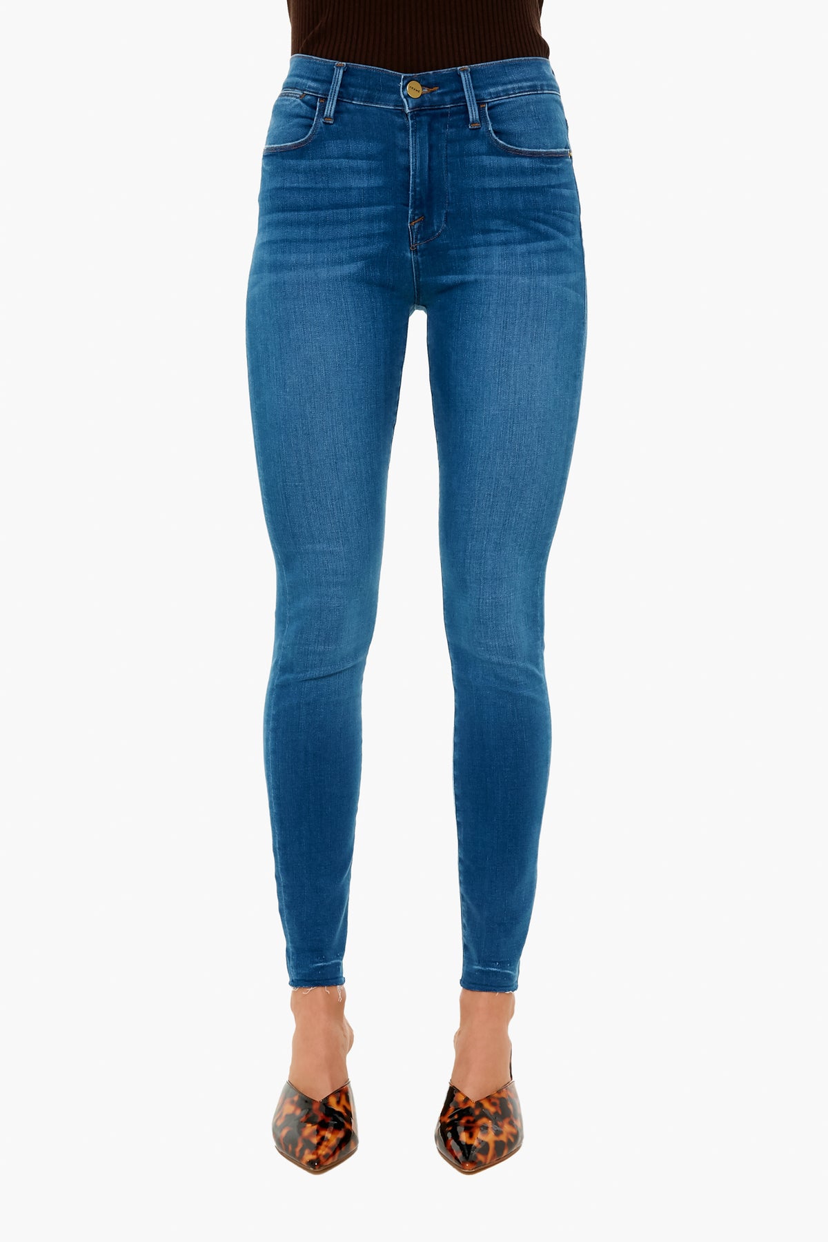 A person wearing FRAME blue high rise skinny jeans crafted from sustainable denim, paired with brown animal print pointed-toe shoes.