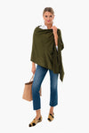 A woman stands confidently in a green breezy Poncho by Pomander Place, white shirt, blue cropped jeans, patterned loafers, and holding a woven handbag.