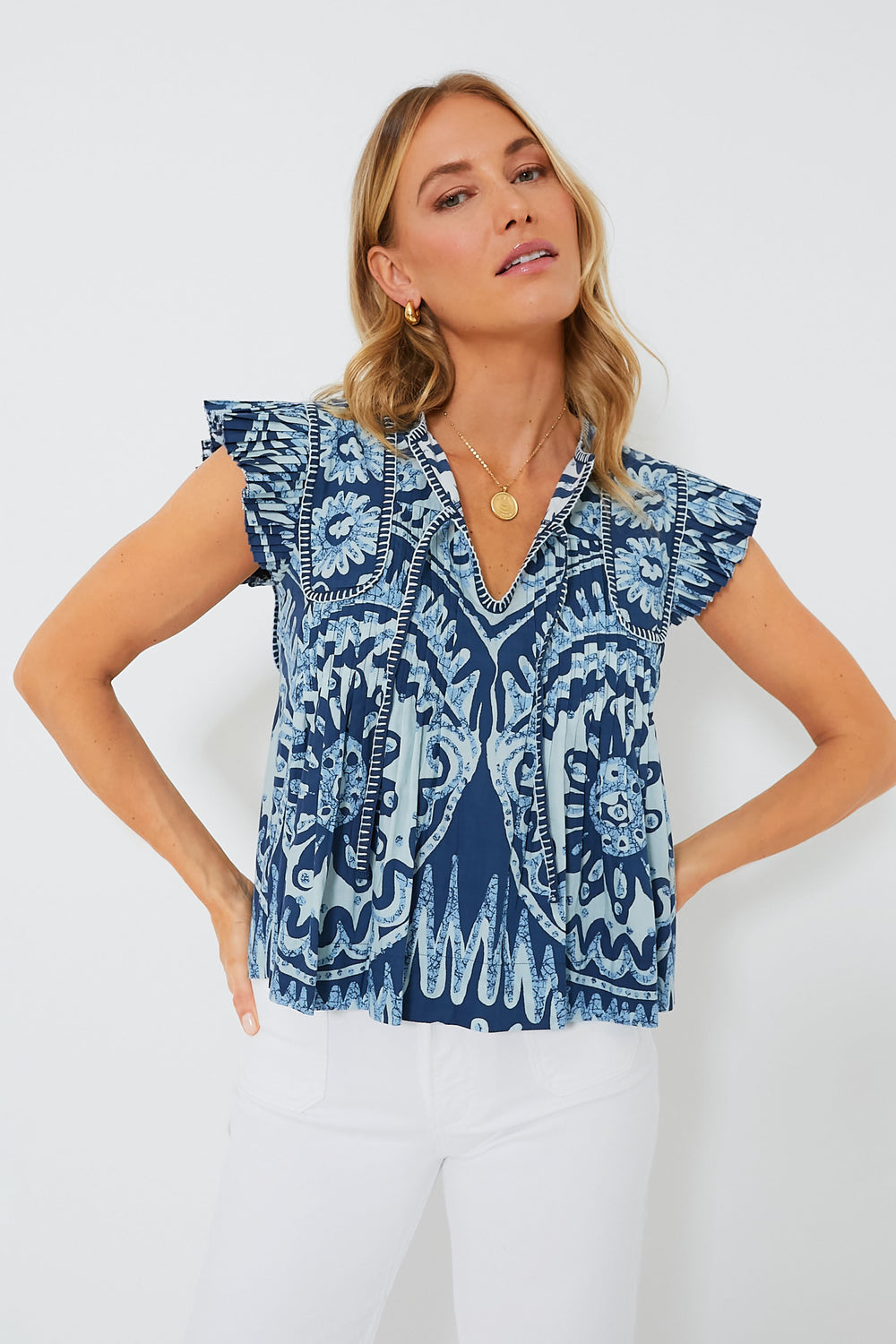 A woman wears a blue patterned Sea New York V-neck tank blouse with white pants, creating a chic and refined look.